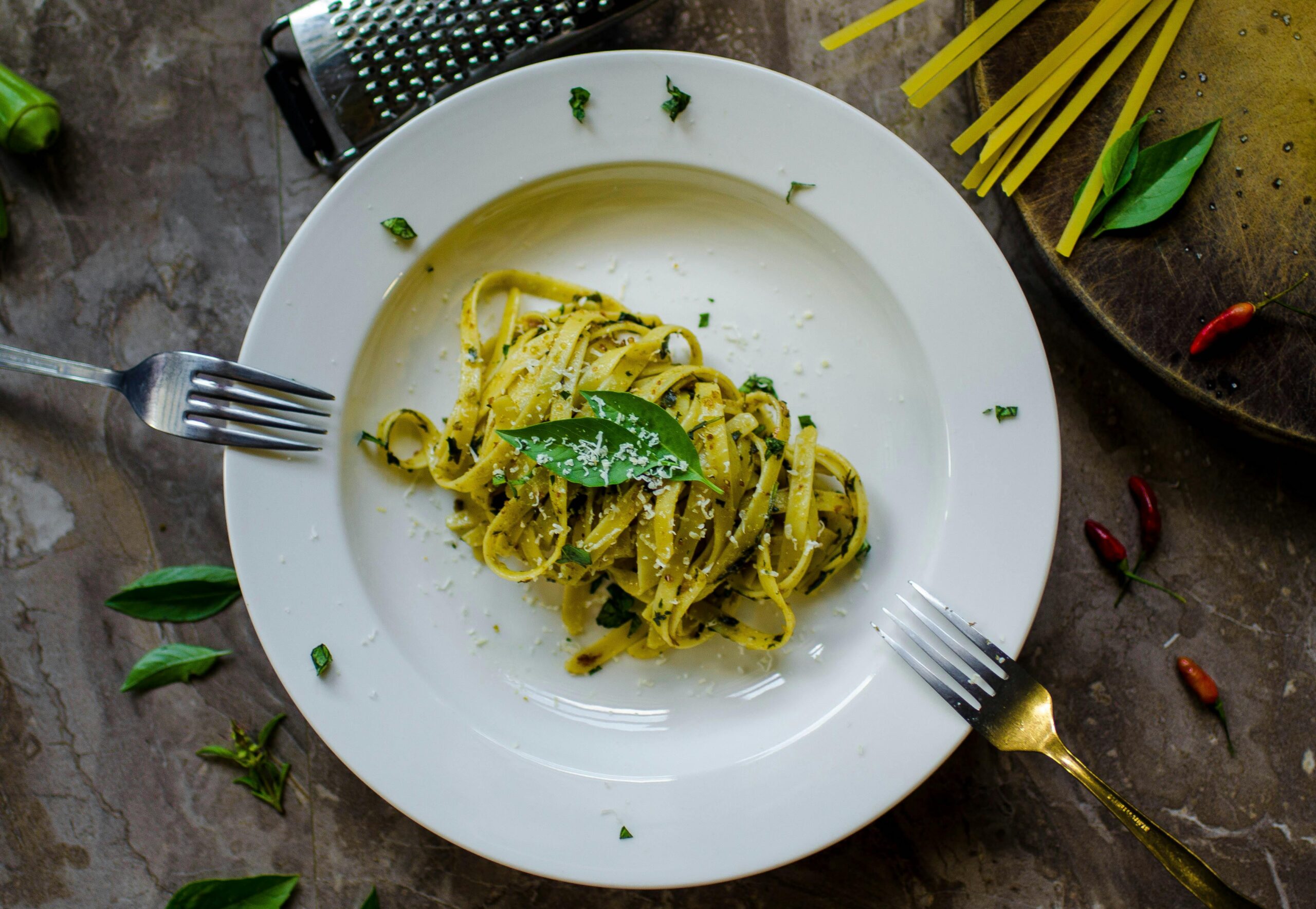 A tempting plate of basil pesto pasta garnished with cheese, surrounded by fresh ingredients.